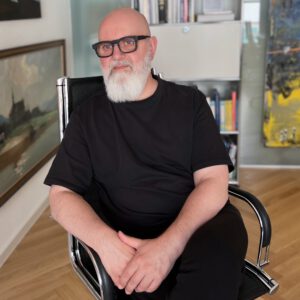 Ein Mann mit grauen Bart und Glatze sitzt auf einem Bürostuhl und schaut in die Ferne