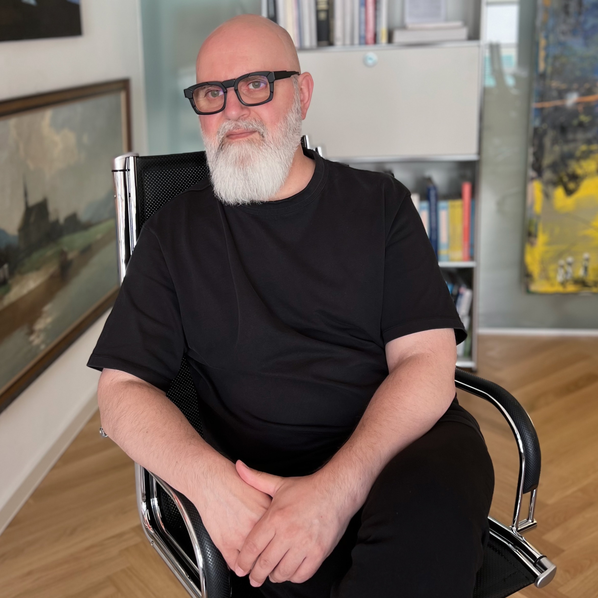 Ein Mann mit grauen Bart und Glatze sitzt auf einem Bürostuhl und schaut in die Ferne